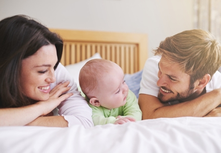 Young couple and their baby smiling on a bed | The Law Offices of Andrea Schneider