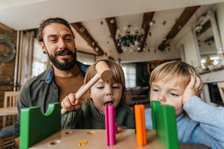 A happy single father watches while his two young children play with a toy. | The Law Offices of Andrea Schneider