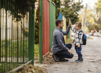 Dad and child high-fiving during a school drop-off on a residential street. | The Law Offices of Andrea Schneider