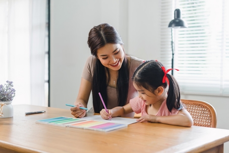 A mother sits with her young daughter, helping her with her homework. | The Law Offices of Andrea Schneider