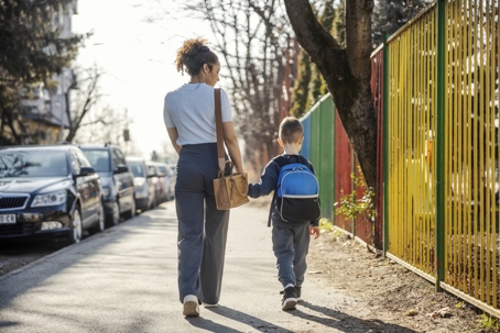 An adult and a child walk along a sidewalk next to a colorful fence. | The Law Offices of Andrea Schneider