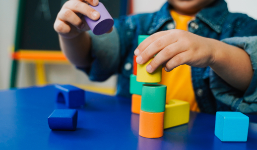 A child stacking colorful wooden blocks on a table. | The Law Offices of Andrea Schneider